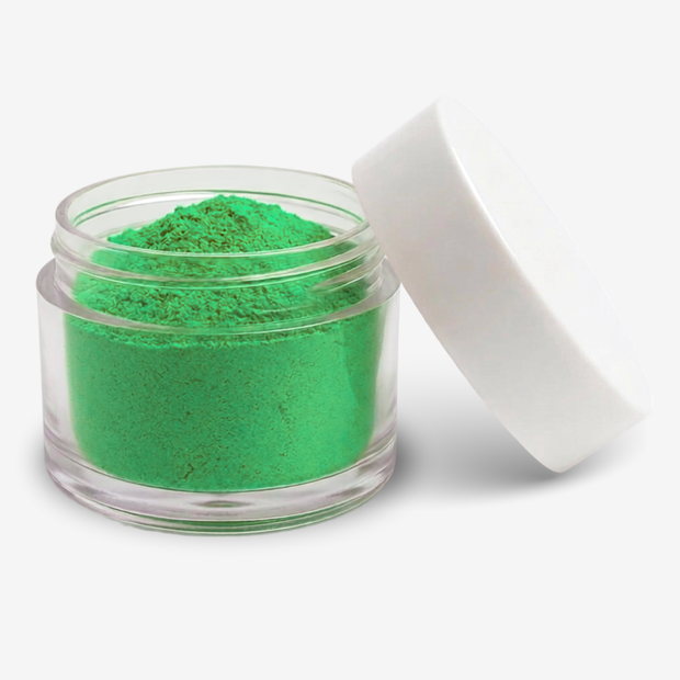 A small clear plastic jar filled with apple green food colouring powder, shown with a white lid leaning against it on a light gray background.