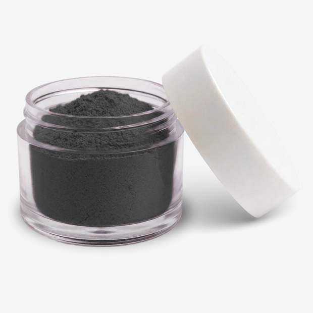 A small clear plastic jar filled with a black food colouring powder, with a white screw-on lid leaning against it on a clean white background.