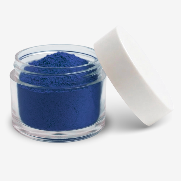 A small clear plastic jar filled with blue food colouring powder, shown with a white screw-on lid leaning against it on a clean white background.