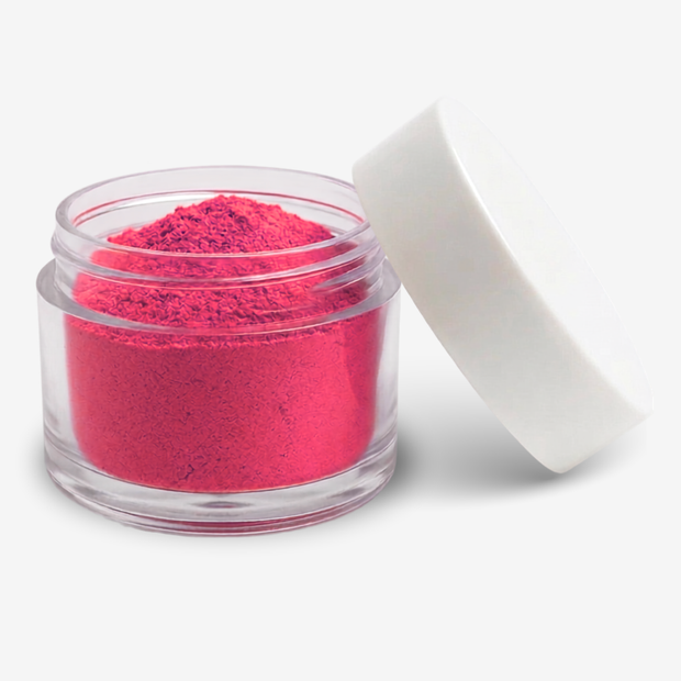 A small clear plastic jar filled with bright hot pink food colouring  powder, shown with its white lid leaning against it on a clean white background.
