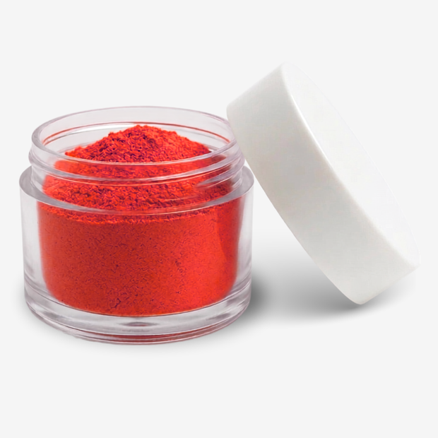 A small clear plastic jar filled with red food colouring powder, shown with its white lid leaning against it on a clean white background.