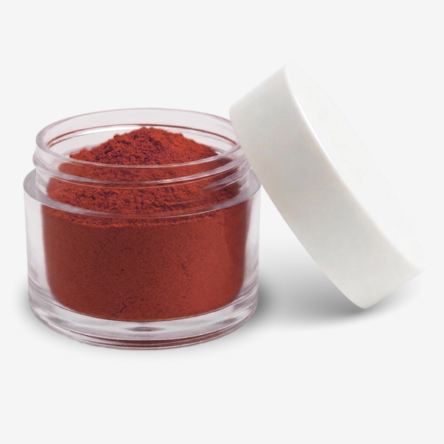 A small clear plastic jar filled with red velvet food colouring powder, shown with its white lid leaning against it on a clean white background.